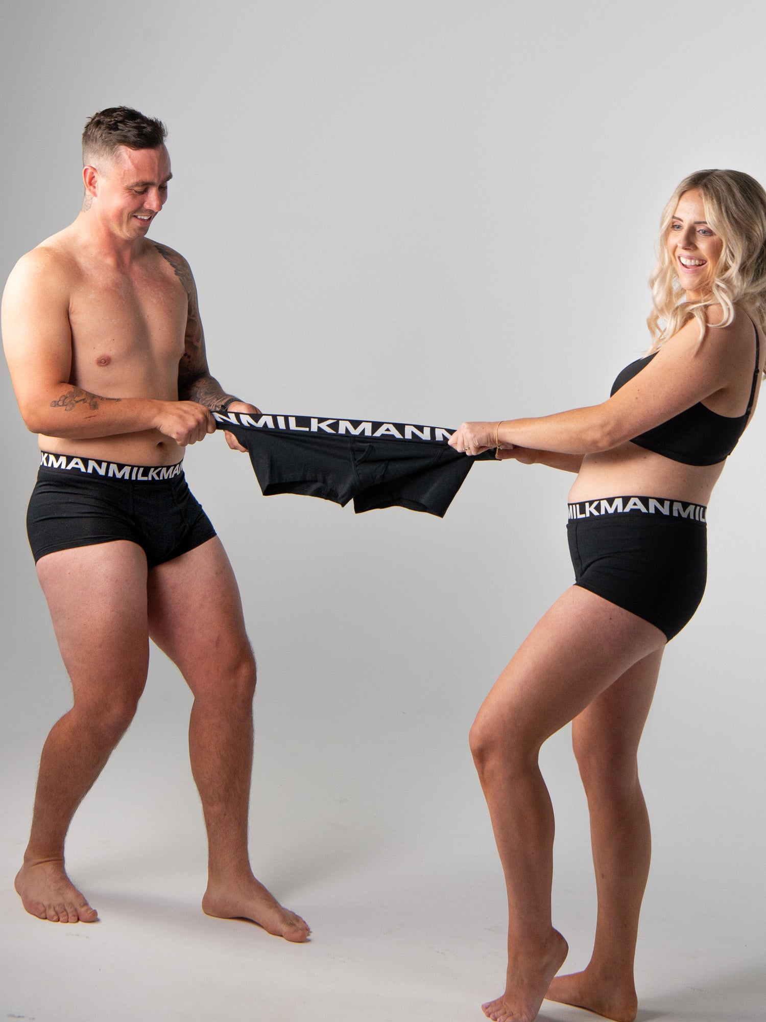 Two people holding black underwear with 'Milkman' branding against a gray background